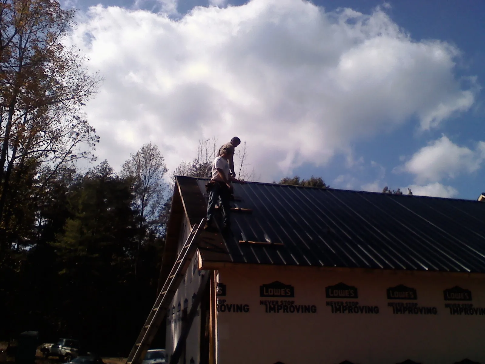Roofer fastening dark metal panels high against a cloudy sky, from a Roof Inspection job in Lynchburg